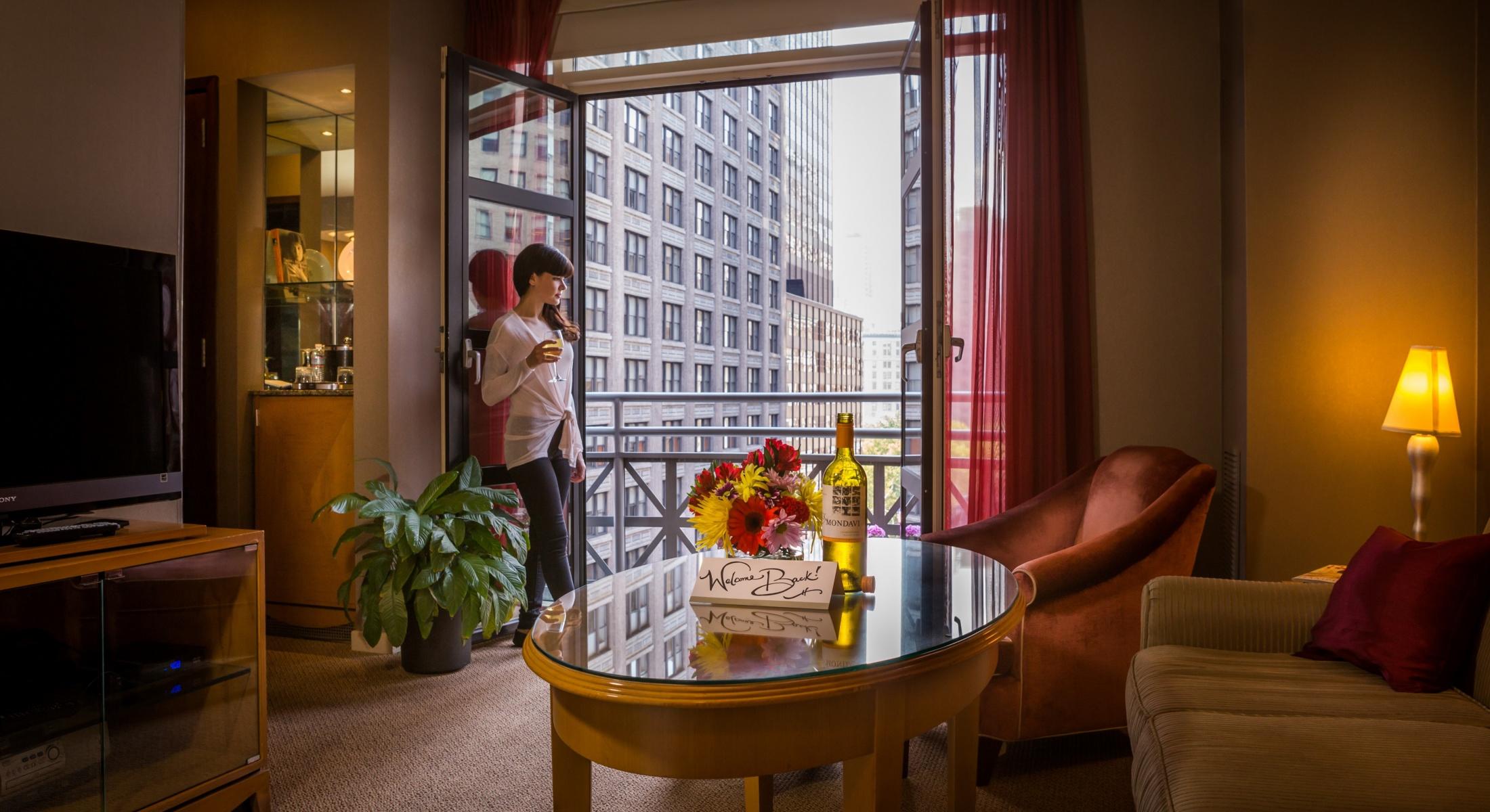 Woman looking out to Park Avenue from the balcony in the living room area of the Balcony King Suite